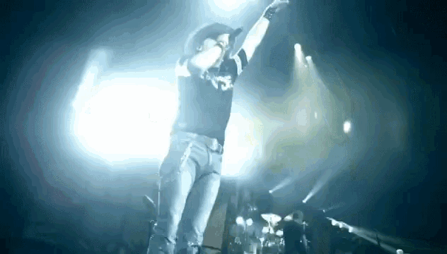 a man in a cowboy hat is singing into a microphone on a stage in front of a crowd .