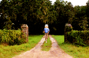 a man is walking down a dirt road wearing a mask