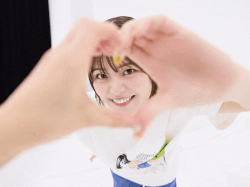 a woman making a heart shape with her hands behind her face