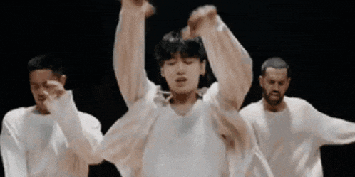 a man in a white shirt is dancing with two other men in white sweaters .