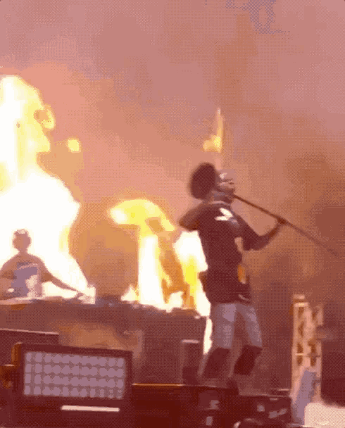 a man stands on a stage holding a microphone in front of flames