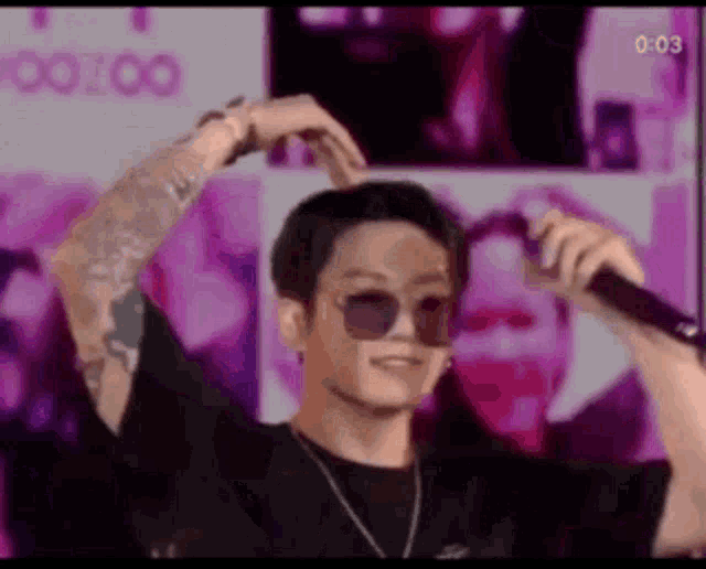 a man wearing sunglasses is holding a microphone and making a heart with his hands .