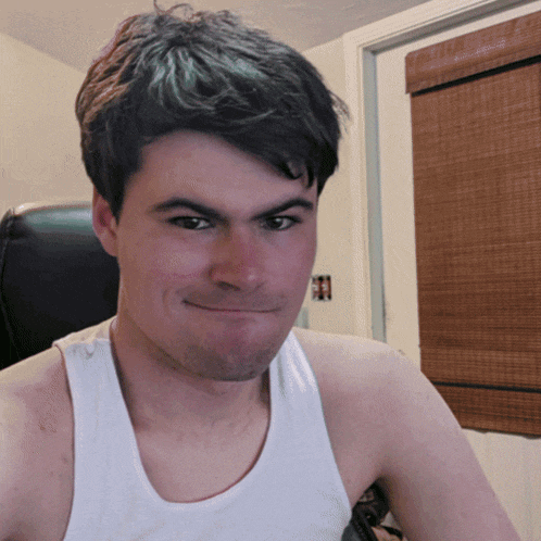 a young man wearing a white tank top is smiling for the camera