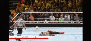 a wrestler is laying on the ground in a wrestling ring while a referee watches .