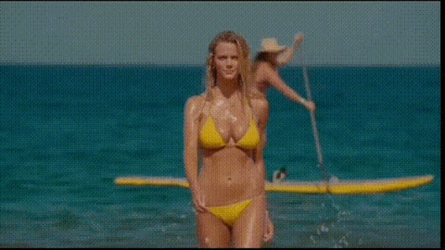 a woman in a yellow bikini is standing on a beach next to a yellow paddle board .