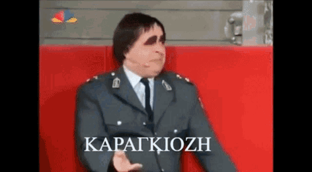 a man in a suit and tie is sitting on a red couch and making a funny face .