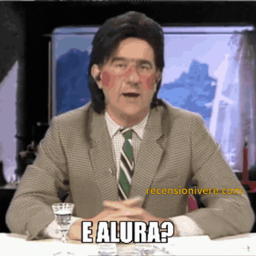 a man in a suit and tie is sitting at a table and says " e alura "