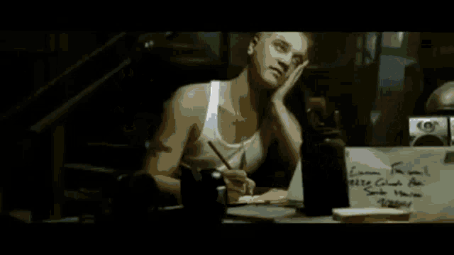 a man in a white tank top is standing in a dark room and looking away from the camera .