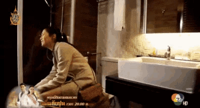 a woman is sitting on a toilet in a bathroom with a tv screen behind her that says ' hd ' on it