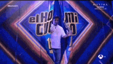 a man in a white shirt is standing in front of a sign that says el ho mi guiso