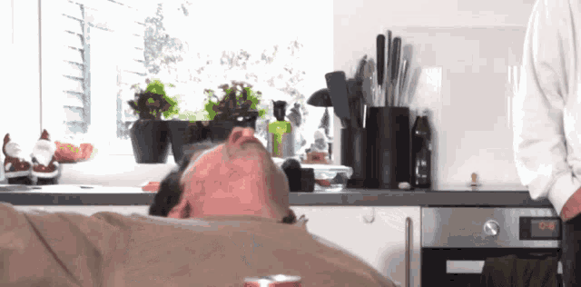 a man laying on a couch in a kitchen with a can of diet coke