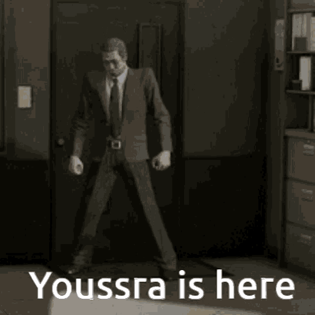a man in a suit and tie is dancing in a dark room with the words youssra is here .