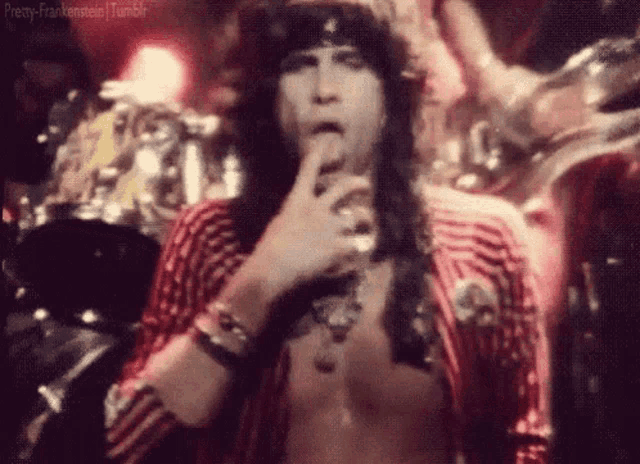 a man without a shirt is holding his hand to his chin and smoking a cigarette in a dark room .