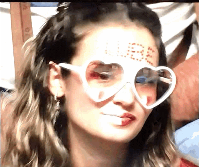 a woman wearing heart shaped sunglasses has the word lose painted on her forehead