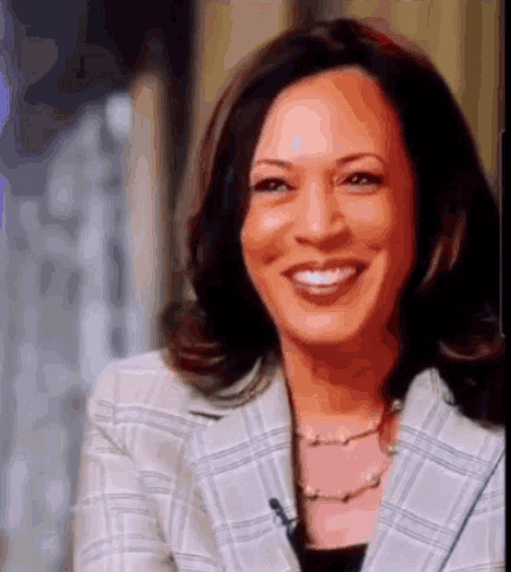 a woman wearing a plaid jacket and a pearl necklace is smiling