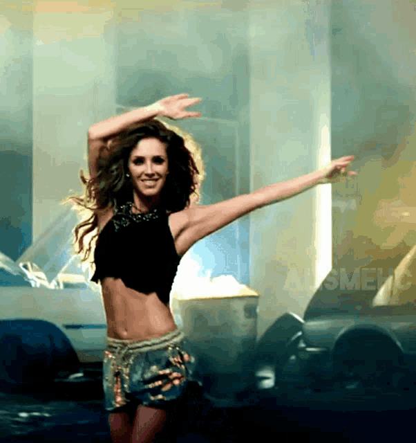 a woman in a crop top and shorts is dancing with her arms outstretched in front of a car