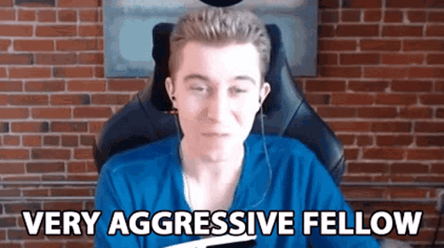 a man in a blue shirt is sitting in front of a brick wall with the words very aggressive fellow below him