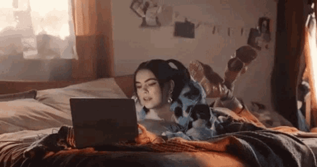 a woman is laying on a bed with her feet up and using a laptop computer .