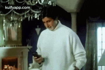 a man in a white sweater is holding a cell phone in his hand .