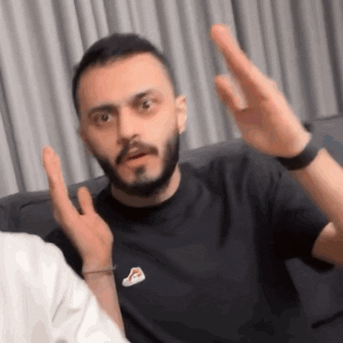 a man with a beard is sitting on a couch and making a funny face with his hands .