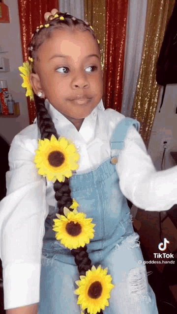a little girl wearing overalls and a braid with sunflowers in it