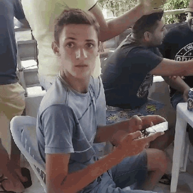 a young man in a blue shirt is sitting in a chair with a can of beer in front of him