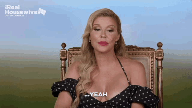 a woman in a black polka dot dress is sitting in a chair and says yeah