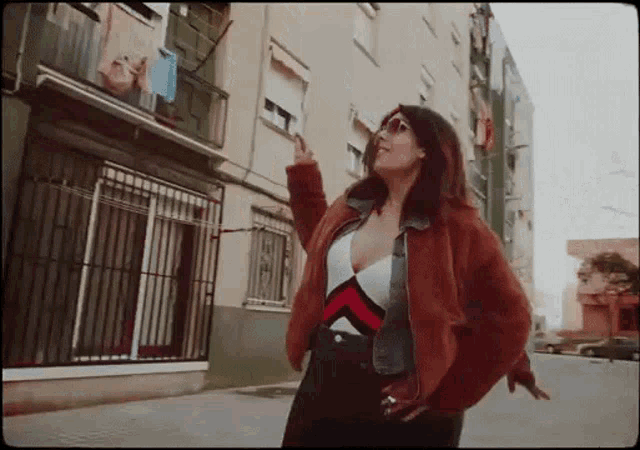 a woman in a red jacket is standing on a street in front of a building