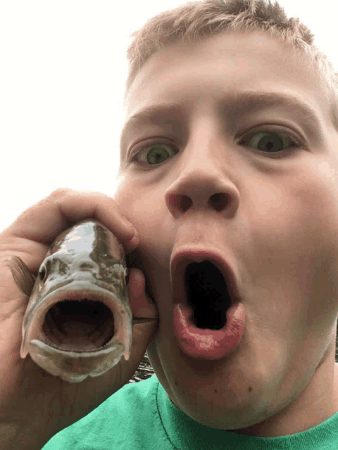 a young boy is holding a fish in his mouth