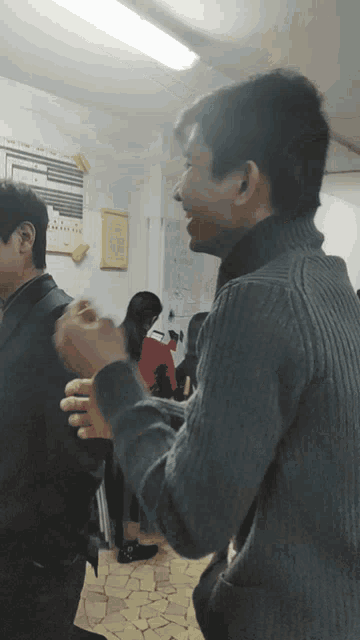 a man in a grey sweater talks to another man in a dark room
