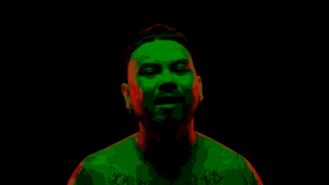 a man with a tattoo on his chest is standing in a dark room with a green light shining on his face .