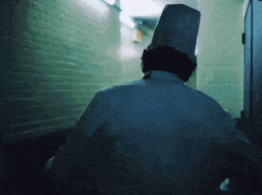 a man in a chef 's hat walks down a hallway