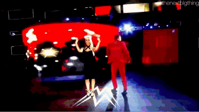 a woman in a black dress stands next to a man in a red suit in front of a large screen that says the next thing
