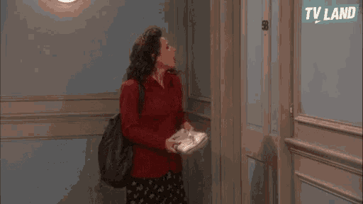 a woman in a red jacket is standing in front of a door holding a newspaper and pointing .