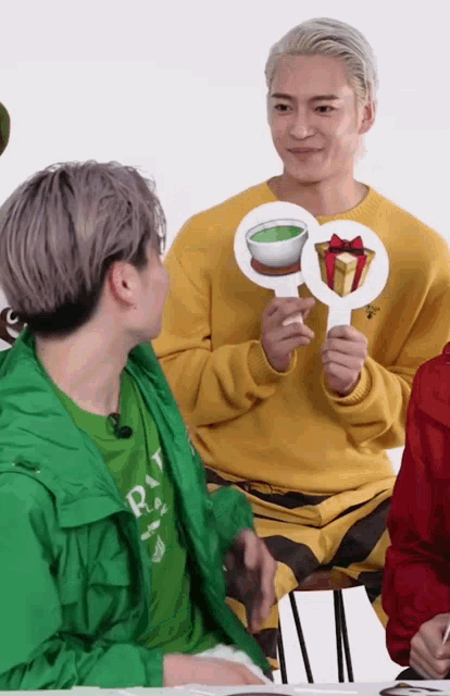 a man in a yellow sweater is holding a sign that has a cup of tea and a gift box on it