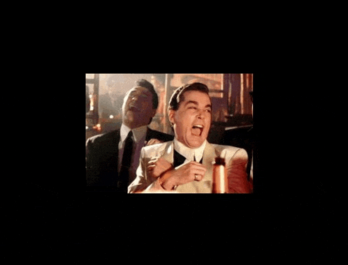 a man in a suit and tie is laughing while another man holds his arm around him .