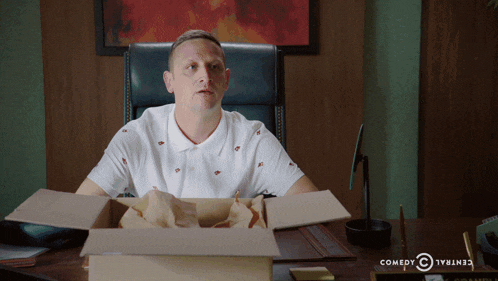 a man sits at a desk with a box in front of him that says comedy central on it