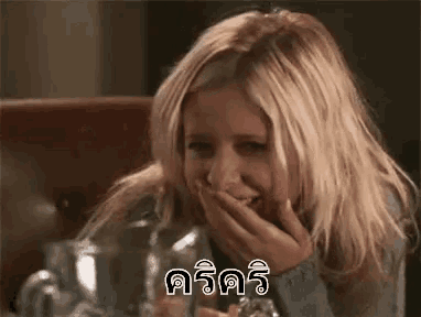 a blonde woman is laughing with her hand over her mouth .