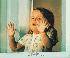a little girl is looking out of a window with her hands up and saying `` love u '' .