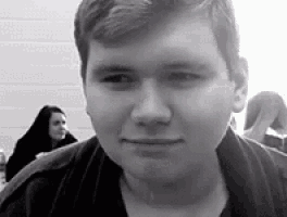 a black and white photo of a young man looking at the camera in a classroom .