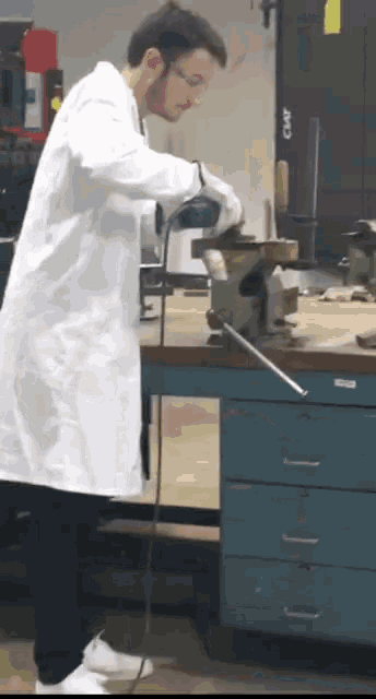 a man in a lab coat is working on a piece of metal in front of a clamp