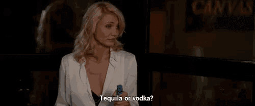 a woman is sitting at a table holding a bottle of tequila and a shot glass .