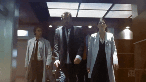 a group of people are walking down a hallway with fox on the bottom right