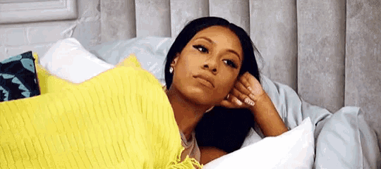 a woman is laying in bed with a yellow pillow and looking at the camera .