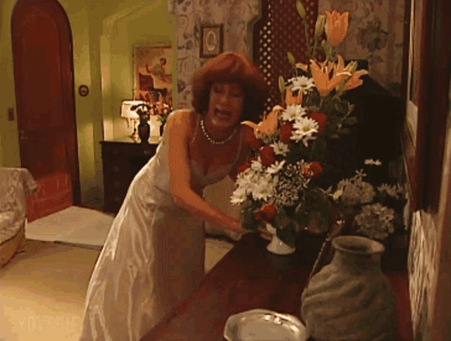 a woman in a white dress is putting flowers into a vase