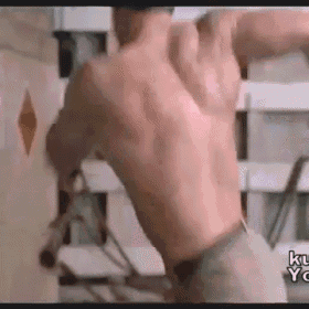 a man without a shirt is standing in front of a wall with his back to the camera .