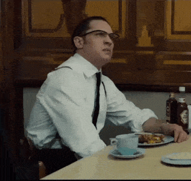 a man wearing glasses sits at a table with a plate of food