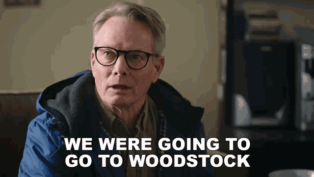 a man wearing glasses and a blue jacket says " we were going to go to woodstock "