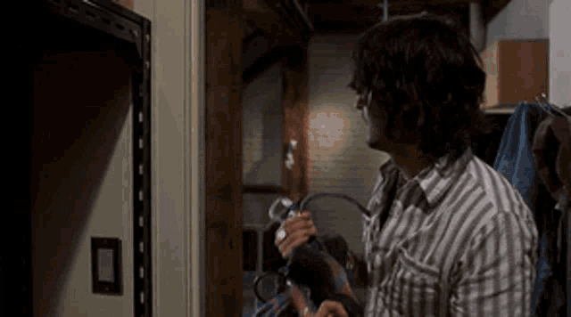 a man in a striped shirt is standing in a closet holding a tool .