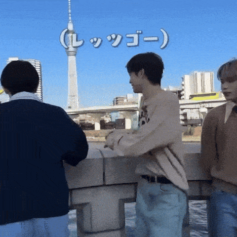 a group of young men are standing on a bridge with a tower in the background and a sign that says " l "